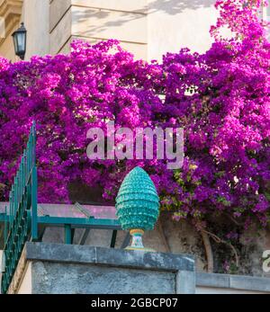 Taormina, Messine, Sicile, Italie. Bougainvillea rose ornant un coin de rue de la vieille ville derrière un vase en céramique exquis sous forme de cône de pin. Banque D'Images