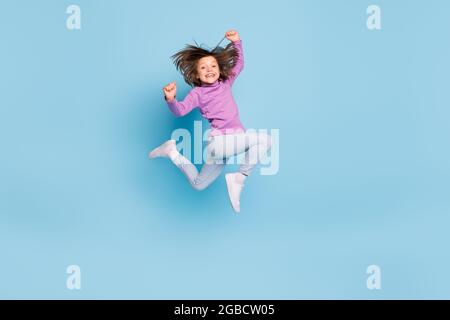 Pleine longueur de taille de corps photo petite fille sautant vers le haut gesturant comme gagnant isolé pastel bleu couleur fond Banque D'Images