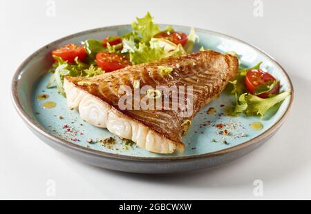 Délicieux steak de poisson frit servi sur une assiette bleue avec des feuilles de salade mélangées et des tomates cerises douces Banque D'Images