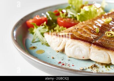 Steak de poisson frit appétissant servi sur une assiette bleue avec des feuilles de salade mélangées et des tomates cerises Banque D'Images