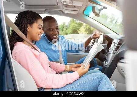 Heureux couple noir regardant la carte papier assis à l'intérieur de la voiture Banque D'Images