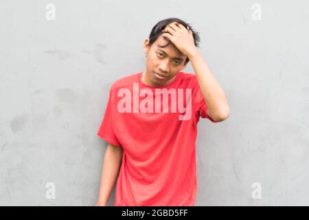 Gros plan d'un jeune homme dans un T-shirt rouge sur le fond d'un mur gris. Banque D'Images
