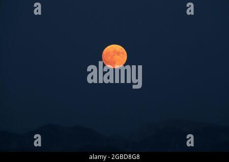 Splendide pleine lune rouge s'élève au-dessus des crêtes de montagne des Apennines. Banque D'Images