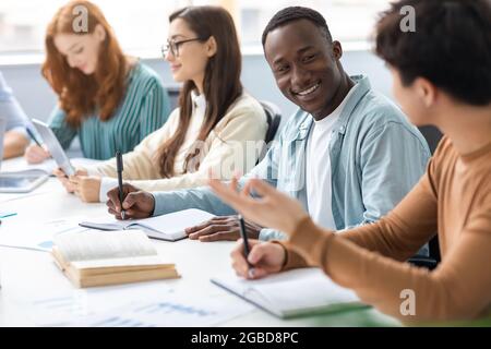 Groupe diversifié d'étudiants assis au bureau écrivant et parlant Banque D'Images