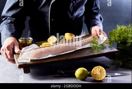 Croissez le chef masculin en uniforme, en montrant du bois avec du filet de poisson biologique non cuit avec des tranches de citron et de l'huile d'olive dans la cuisine Banque D'Images