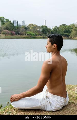 Jeune homme brésilien assis regardant le lac en position de méditation (photo verticale). Banque D'Images