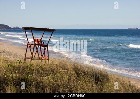 Un stand rouge de sauveteurs sur une plage ensoleillée surplombe une mer bleue calme entourée par la nature dans ce paysage. Banque D'Images