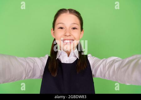 Photo portrait écolière souriante gaie prenant selfie dans uniforme isolé pastel couleur vert fond. Banque D'Images