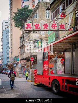 HONG KONG, HONG KONG - 24 juillet 2018 : un camion de livraison Coca Cola rouge vif est déchargé sous un panneau de néon chinois rouge sur une rue de Hong Kong... haut Banque D'Images