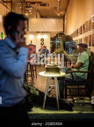 HONG KONG, HONG KONG - 24 juillet 2018 : un homme sur un téléphone portable qui passe devant la fenêtre d'un ancien magasin de disques où les hommes s'assoyent à écouter Banque D'Images