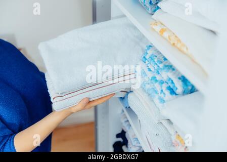Femme mains tenant les serviettes et les mettant sur une étagère sur le tiroir de l'armoire lors du nettoyage général par le système de stockage moderne. Concept de confort Banque D'Images