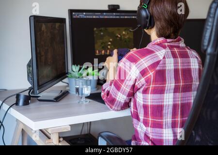 Retour Voir la femme dans un casque avec une manette Xbox jouant à des jeux vidéo sur son PC de bureau. Temps en ligne, vie virtuelle, addiction aux jeux. Mise au point sélective. Banque D'Images