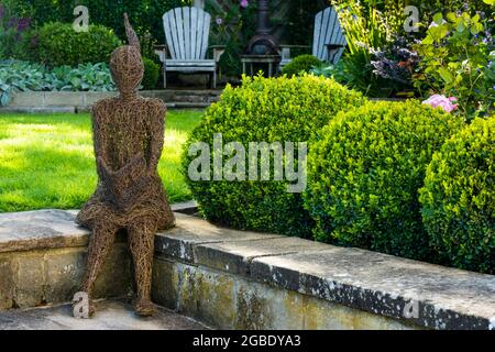 Sculpture (élément ornemental) dans un beau jardin paysagé (plantes vivaces, arbustes, balles en forme de boîte, pelouse, chaises) - Yorkshire Angleterre Royaume-Uni Banque D'Images