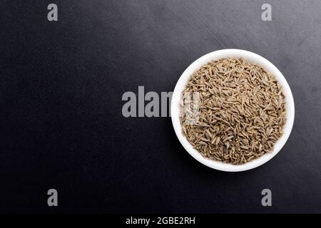 Vue de dessus des graines de cumin dans le bol sur fond sombre Banque D'Images