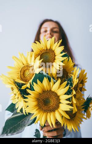 Jeune jolie femme tenant un bouquet de tournesols sur un fond blanc. Composition florale minimale. Photo de haute qualité Banque D'Images