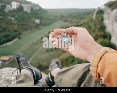 L'homme est assis au bord d'une falaise et tient un compas dans la vue d'arrière-plan du canyon. Banque D'Images