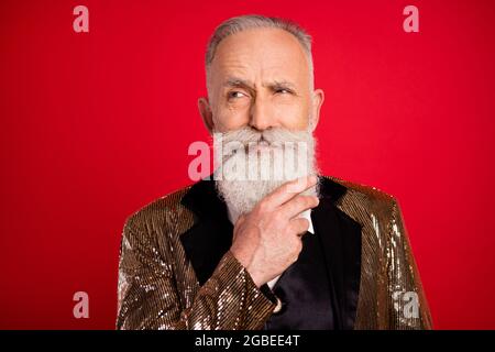 Portrait de personnes âgées de classe attirantes méfiant homme à cheveux gris surestimé touchant la barbe isolée sur fond rouge vif Banque D'Images