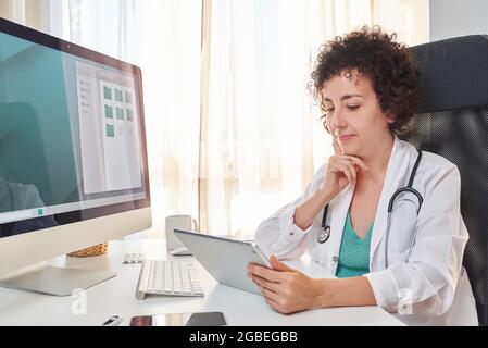 Une femme médecin utilise sa tablette numérique, assise au bureau de son bureau médical Banque D'Images