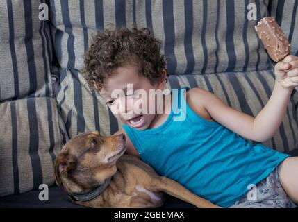 chiot allongé sur le canapé avec un enfant tenant une glace au chocolat dans sa main Banque D'Images