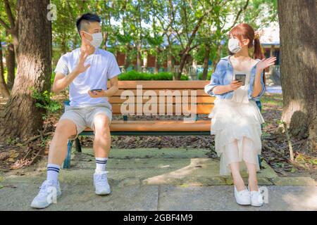 Jeune couple en prise de distance sociale et assis sur le banc dans le parc Banque D'Images