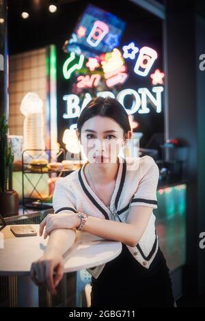 Jeune femme chinoise assise à une table avec des néons en arrière-plan à Chengdu, province du Sichuan, en Chine Banque D'Images