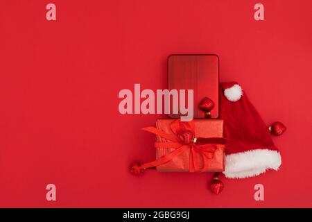 Vue de dessus de la composition du chapeau de père Noël traditionnel placé près des cadeaux emballés le jour de Noël sur fond rouge Banque D'Images