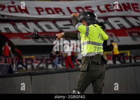 Un policier utilise son bâton pour retenir les supporters de l'équipe de Santa Fe Independiente comme les pendentifs et les signes de l'équipe sont vus dans le dos comme les partisans de l'Independiente Santa Fe inondent le terrain du stade Nemesio Camacho el Campin après les partisans de l'équipe Atletico Nacional Violemment attaqué les supporters de Santa Fe dans une tribune provoquant la suspension du premier match de football avec des fans à Bogota, Colombie, le 3 août 2021. Banque D'Images