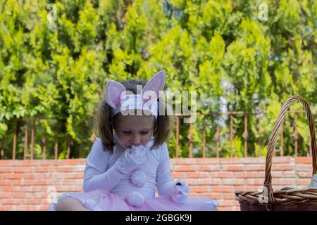 une petite fille en costume de lapin a un pique-nique dans le jardin de sa maison. Banque D'Images