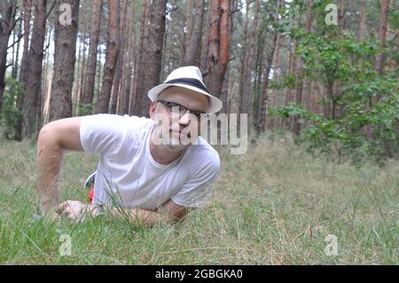 Jeune homme en chapeau et en forêt, allongé sur le sol de la forêt, profitant de la vie. Style de vie. Banque D'Images