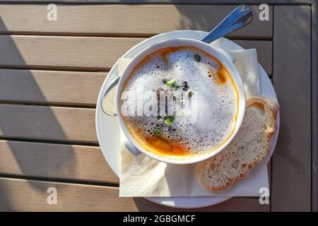 Soupe de légumes avec des pousses fraîches et garniture en mousse comme apéritif dans un menu extérieur sur une table de jardin en bois, espace de copie, vue d'en haut, s Banque D'Images