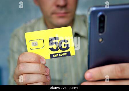 Un homme tient une carte SIM jaune avec l'inscription 5G et un téléphone portable dans sa main. Remplacement de la carte SIM et passage à Internet haut débit. Banque D'Images