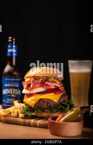 Hamburger appétissant avec des frites et de la bière sur une planche de bois sur fond noir Banque D'Images