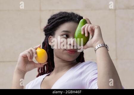 Femme africaine avec avocat et citron dans ses mains. Avocat sur le fond de l'oeil d'une femme. Publicité de fruits pour promouvoir les vitamines. Couleur dégradée Banque D'Images