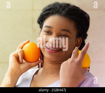 Jeune femme afro gaie avec de l'orange et du citron dans ses mains. Promotion de modes de vie sains Banque D'Images