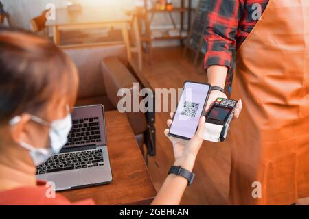 Femme effectuant un paiement mobile sur un lecteur de carte dans un café Banque D'Images