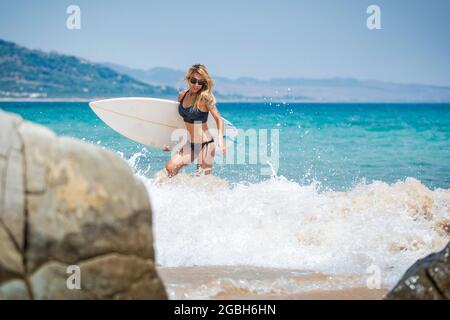 Femme marchant hors de la mer portant sa planche de surf, plage de Punta Paloma, Tarifa, Cadix, Andalousie, Espagne Banque D'Images