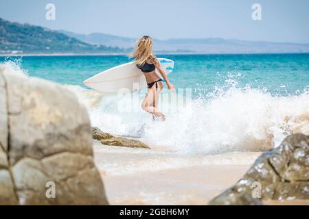 Femme marchant hors de la mer portant sa planche de surf, plage de Punta Paloma, Tarifa, Cadix, Andalousie, Espagne Banque D'Images