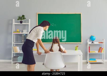 Une enseignante aidant une petite fille à suivre une leçon de mathématiques en classe. Le tuteur et l'élève travaillent ensemble pendant la classe à l'école Banque D'Images