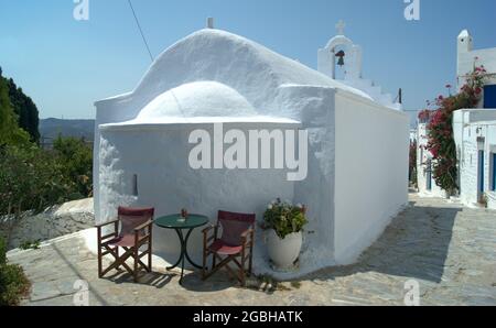 Belle église grecque, île d'Amorgos, Cyclades, Grèce. Tables et chaises près du charmant bâtiment ancien et traditionnel, sur la place du village. Banque D'Images