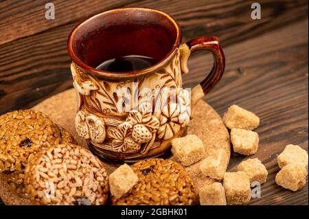 Biscuits faits maison avec graines de tournesol et raisins secs, morceaux de sucre de canne brun et une tasse de thé en faïence sur une table en bois. Gros plan focau sélectif Banque D'Images