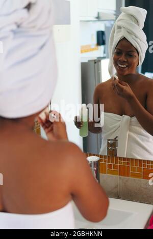 Une femme africaine nettoie son visage le matin, debout devant un miroir. Banque D'Images