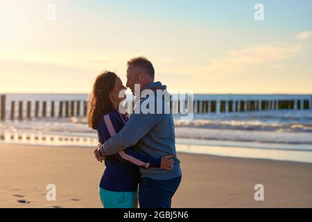 Couple romantique d'âge moyen qui s'embrasse sur une plage tropicale au coucher du soleil en regardant avec amour les autres yeux avec un espace de copie latéral Banque D'Images