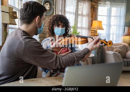 Une femme heureuse joue du violon sous les instructions d'un professeur de musique dans un masque pendant le coronavirus à la maison Banque D'Images