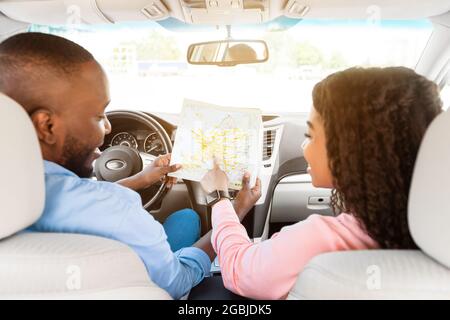 Heureux couple noir regardant la carte assis à l'intérieur de la voiture Banque D'Images