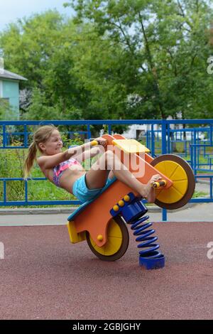 Une jeune fille de 9 ans est assise sur un jouet moto en bois avec le printemps sur l'aire de jeux Banque D'Images