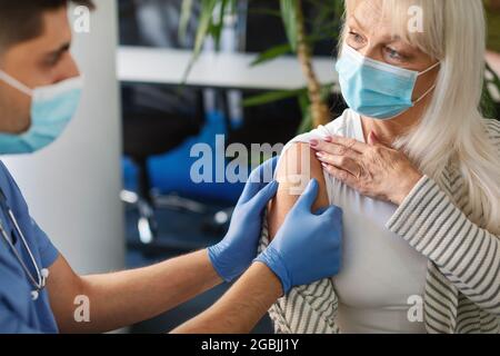 Femme âgée se faire vacciner contre Covid-19, docteur appliquant le bandage Banque D'Images