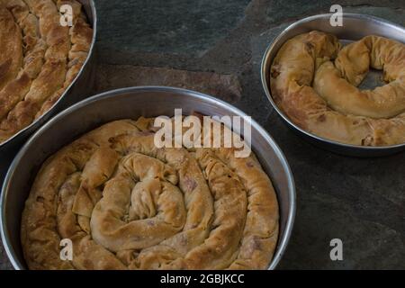 Tarte traditionnelle au fromage grec maison tortillé dans trois plats en fer avec filo, épinards, mizithra et feta. Banque D'Images
