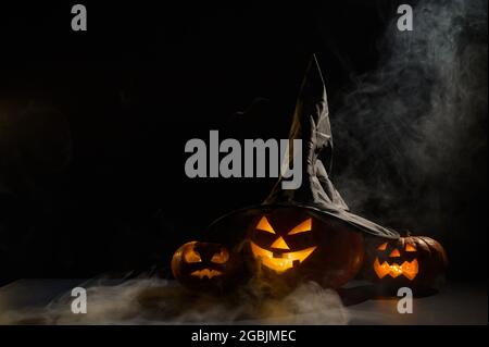 Les citrouilles d'orange effrayantes pour Halloween sont rangées sur un fond sombre. Jack O Lantern dans un chapeau de sorcière. Le brouillard mystique avance sur le sol. Trick or Banque D'Images