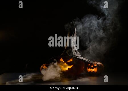 Les citrouilles d'orange effrayantes pour Halloween sont rangées sur un fond sombre. Jack O Lantern dans un chapeau de sorcière. Le brouillard mystique avance sur le sol. Trick or Banque D'Images