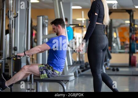 Un homme est engagé dans une salle de gym sur un simulateur avec une fille comme instructeur. Banque D'Images